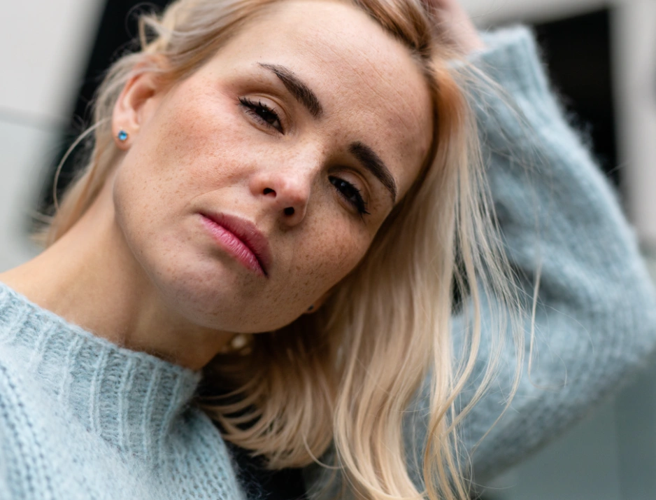 eine junge Frau mit feinem blonden Haar schaut kritisch in die Kamera.